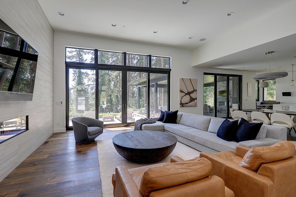Photo of a large contemporary open concept living room in Portland with grey walls, medium hardwood floors, a ribbon fireplace, a plaster fireplace surround, a wall-mounted tv and brown floor.