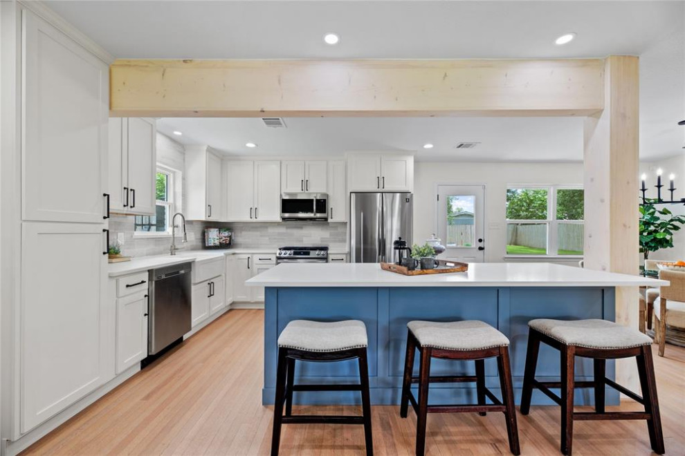 This is an example of a small eclectic l-shaped open plan kitchen in Houston with white cabinets, grey splashback, stainless steel appliances, an island and beige floors.