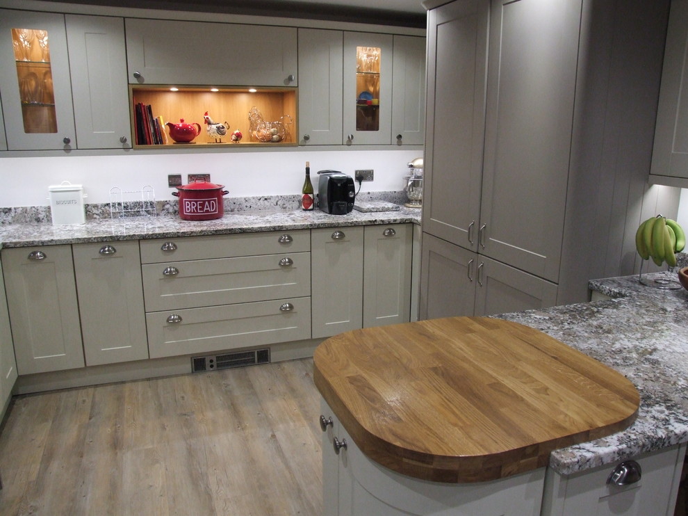 Photo of a mid-sized traditional u-shaped eat-in kitchen in Dorset with a drop-in sink, shaker cabinets, beige cabinets, granite benchtops, beige splashback, terra-cotta splashback, black appliances, vinyl floors and a peninsula.