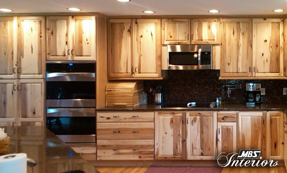 Example of a mountain style l-shaped eat-in kitchen design with raised-panel cabinets, light wood cabinets, quartzite countertops, black backsplash and stainless steel appliances