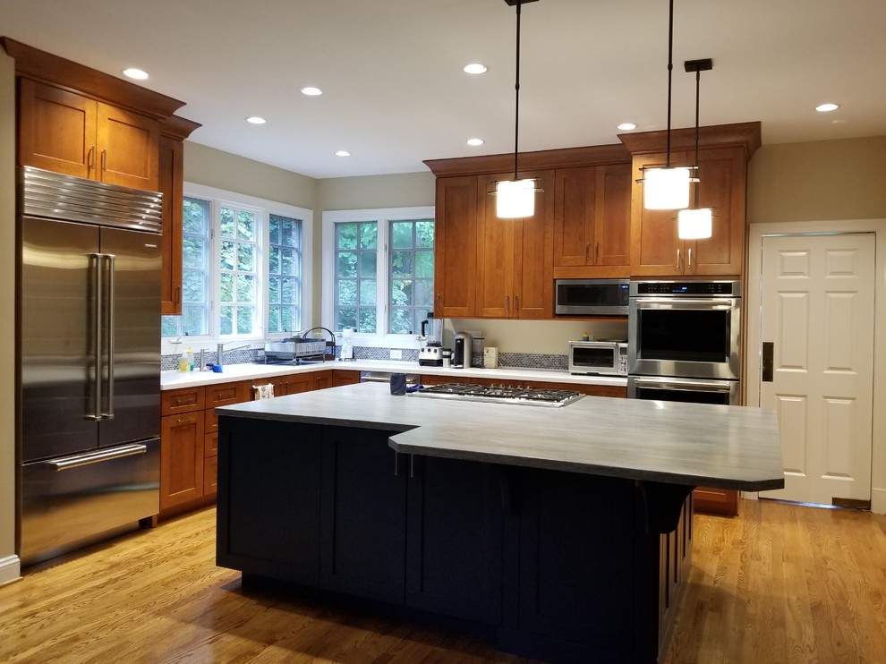 Photo of a mid-sized transitional l-shaped eat-in kitchen in DC Metro with an integrated sink, recessed-panel cabinets, medium wood cabinets, solid surface benchtops, blue splashback, mosaic tile splashback, stainless steel appliances, medium hardwood floors, a peninsula, brown floor and blue benchtop.