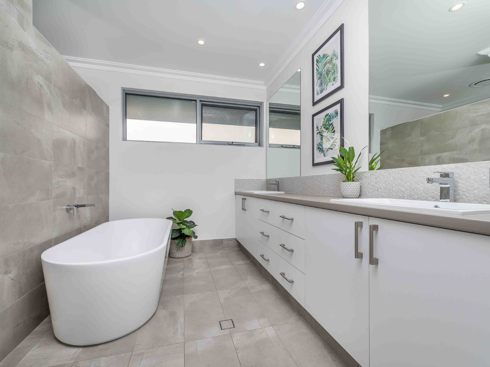 Large contemporary bathroom in Perth with flat-panel cabinets, white cabinets, a freestanding tub, porcelain tile, white walls, a drop-in sink, white benchtops, gray tile and grey floor.