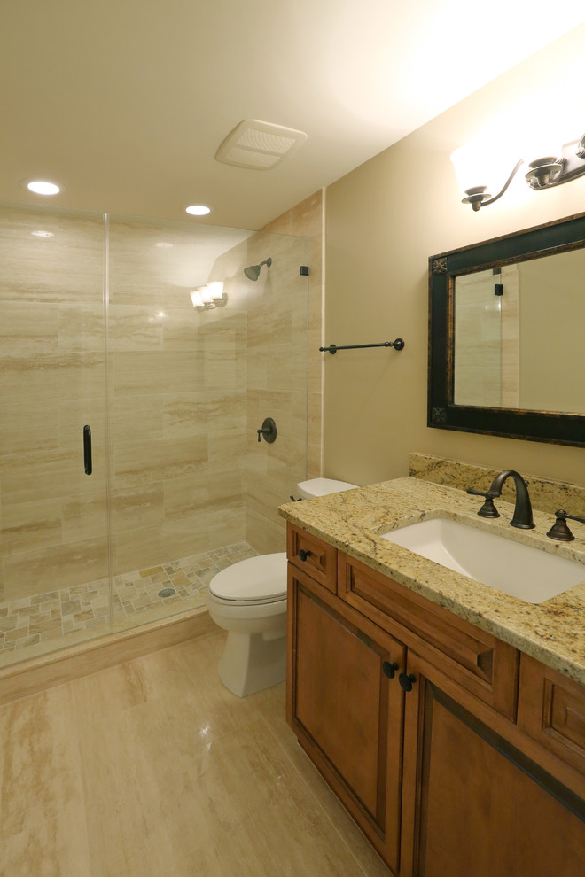 Photo of a mid-sized mediterranean bathroom in Tampa with raised-panel cabinets, medium wood cabinets, an open shower, a one-piece toilet, beige tile, brown tile, gray tile, stone tile, beige walls, marble floors, an undermount sink and granite benchtops.