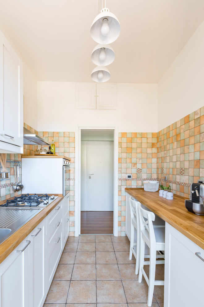 Mid-sized mediterranean galley separate kitchen in Rome with a drop-in sink, beaded inset cabinets, white cabinets, wood benchtops, multi-coloured splashback, ceramic splashback, ceramic floors, stainless steel appliances and beige floor.