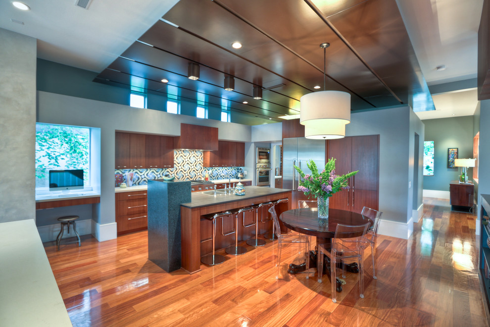 This is an example of a large contemporary l-shaped open plan kitchen in Houston with a double-bowl sink, flat-panel cabinets, dark wood cabinets, soapstone benchtops, multi-coloured splashback, mosaic tile splashback, stainless steel appliances, medium hardwood floors, with island and brown floor.