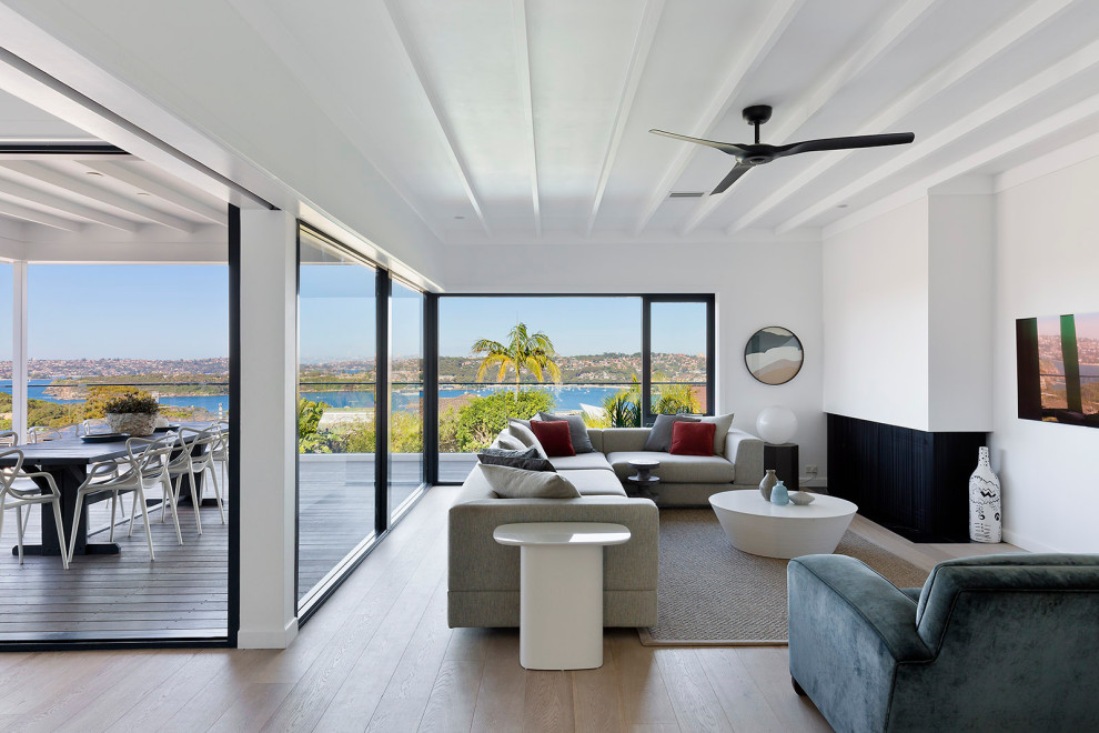 Großes, Offenes Maritimes Wohnzimmer mit weißer Wandfarbe, hellem Holzboden, Eckkamin, TV-Wand, beigem Boden und freigelegten Dachbalken in Sydney