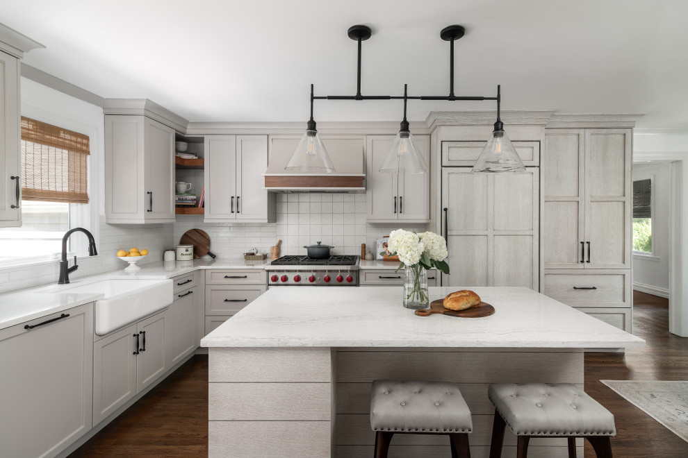 Eat-in kitchen - mid-sized transitional l-shaped medium tone wood floor and brown floor eat-in kitchen idea in New York with a farmhouse sink, shaker cabinets, beige cabinets, quartz countertops, white backsplash, porcelain backsplash, paneled appliances, an island and white countertops