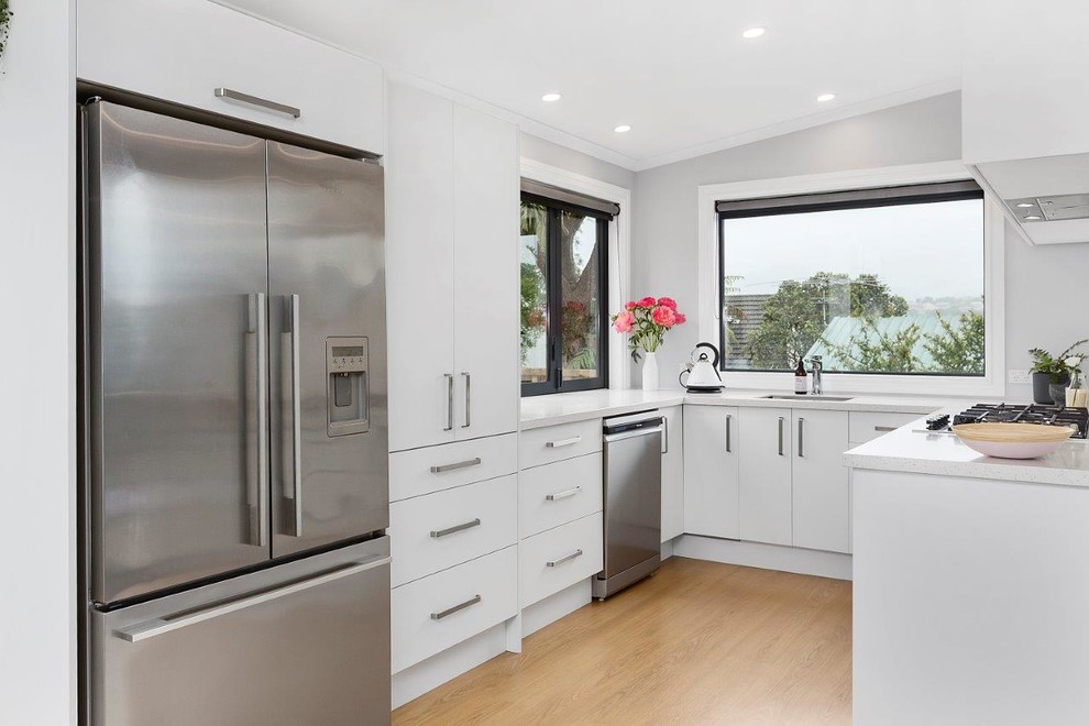 Scandinavian u-shaped kitchen in Other with a drop-in sink, white cabinets, white splashback, ceramic splashback, stainless steel appliances, laminate floors and brown floor.