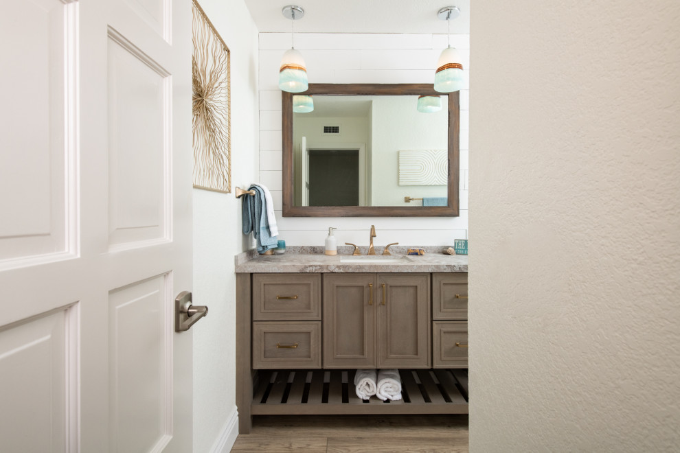 Photo of a mid-sized beach style 3/4 bathroom in Orange County with recessed-panel cabinets, a freestanding tub, an alcove shower, a one-piece toilet, beige tile, porcelain tile, white walls, an undermount sink, engineered quartz benchtops, multi-coloured benchtops, an enclosed toilet, a built-in vanity, brown cabinets, brown floor, a single vanity, a sliding shower screen and panelled walls.