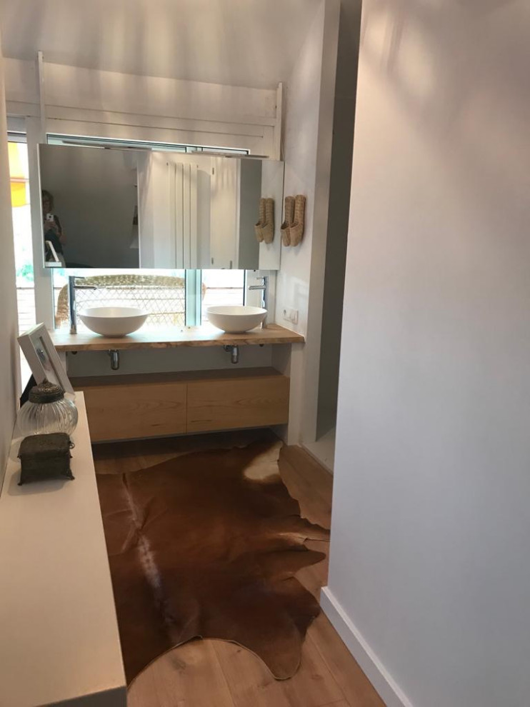 This is an example of a large mediterranean master bathroom in Barcelona with furniture-like cabinets, light wood cabinets, a curbless shower, a wall-mount toilet, white walls, light hardwood floors, a vessel sink, wood benchtops, beige floor, an open shower, beige benchtops, a double vanity and a floating vanity.