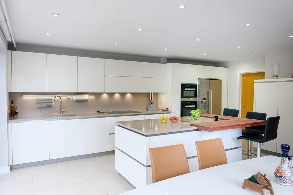 Inspiration for a mid-sized modern open plan kitchen in Surrey with flat-panel cabinets, white cabinets, limestone benchtops, stainless steel appliances, limestone floors, a peninsula, beige floor and beige benchtop.