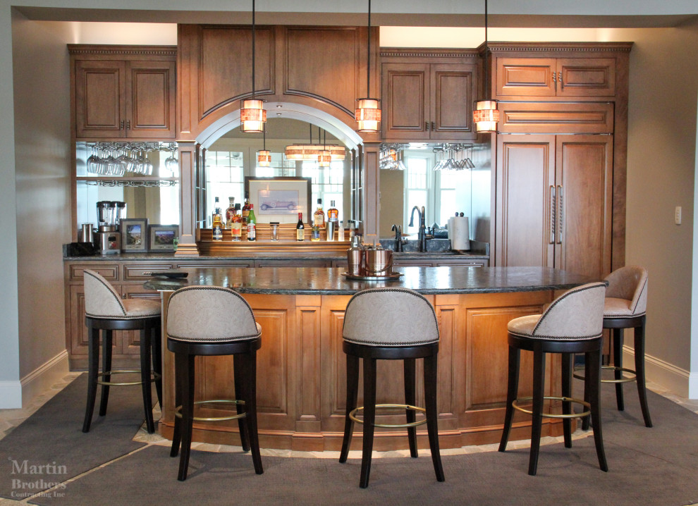 Photo of an expansive traditional single-wall seated home bar in Other with an undermount sink, raised-panel cabinets, medium wood cabinets, granite benchtops, mirror splashback and slate floors.