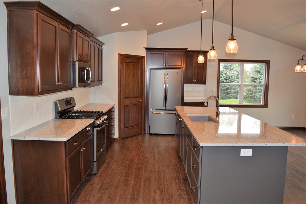 Example of a light wood floor open concept kitchen design with an undermount sink, flat-panel cabinets, dark wood cabinets, granite countertops, white backsplash, ceramic backsplash, stainless steel appliances and an island