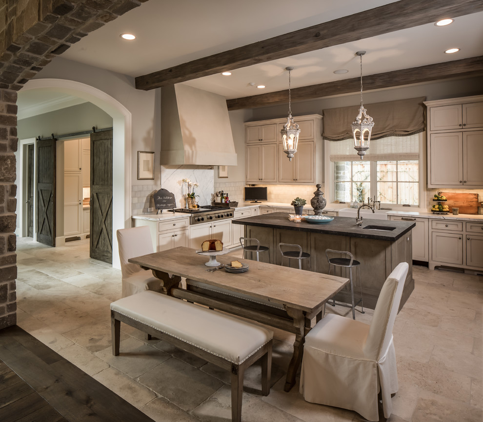 Mid-sized traditional u-shaped eat-in kitchen in Houston with a farmhouse sink, recessed-panel cabinets, stainless steel appliances, white splashback, limestone splashback, white cabinets, quartzite benchtops, limestone floors, with island and beige floor.