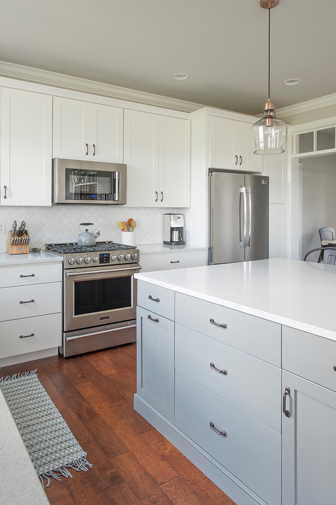 Inspiration for a mid-sized transitional l-shaped medium tone wood floor and brown floor open concept kitchen remodel with a farmhouse sink, shaker cabinets, white cabinets, quartzite countertops, white backsplash, subway tile backsplash, stainless steel appliances and an island