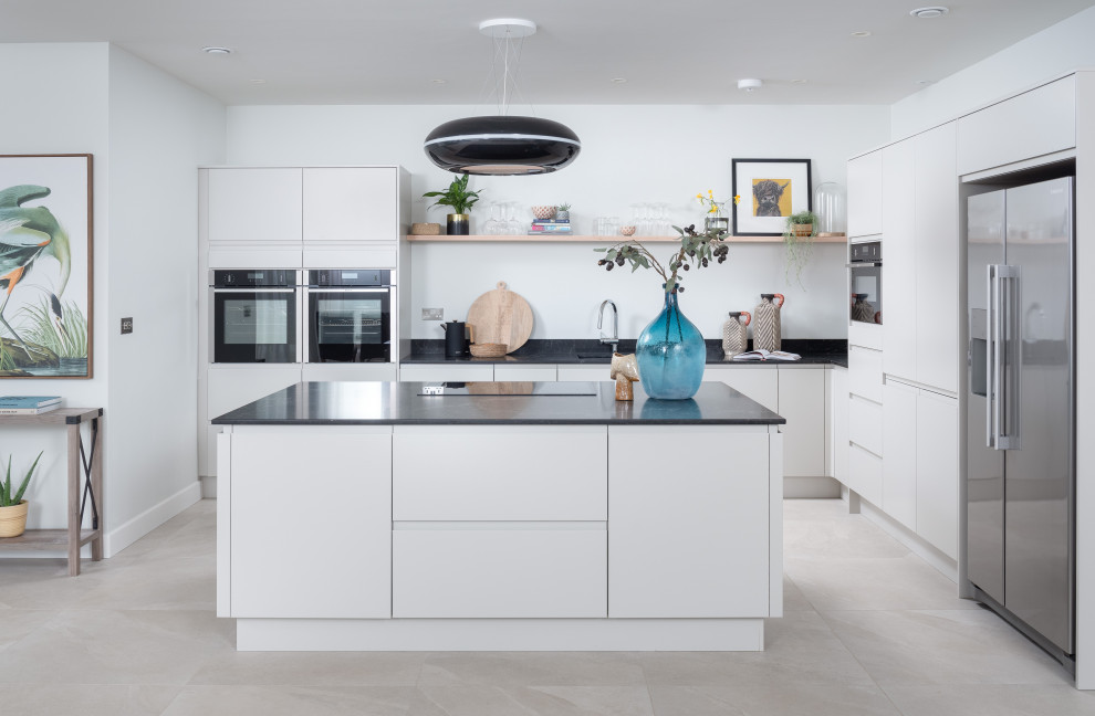 Photo of a coastal open plan kitchen in Dorset with flat-panel cabinets, black cabinets, granite worktops, an island and grey floors.