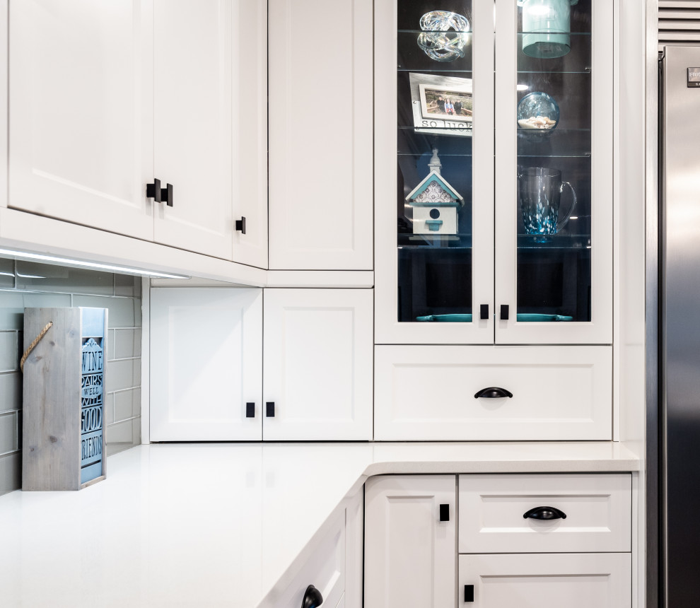 Large transitional l-shaped medium tone wood floor and brown floor kitchen photo with an undermount sink, white cabinets, quartz countertops, white backsplash, glass tile backsplash, stainless steel appliances, an island and white countertops