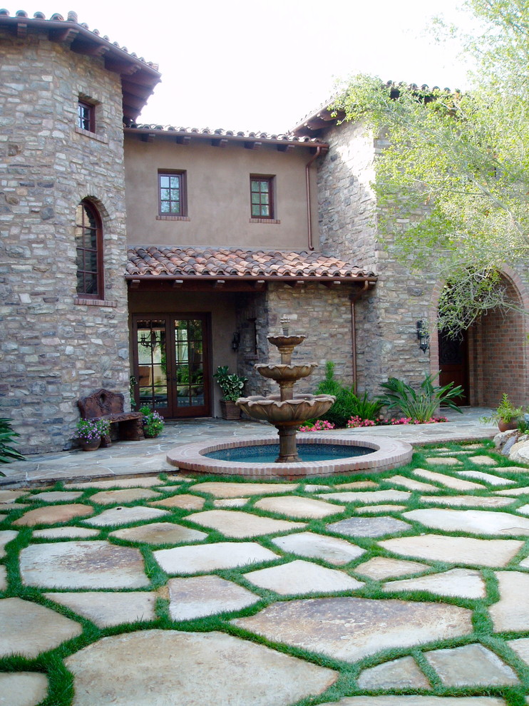 This is an example of an expansive mediterranean courtyard patio in San Diego with a water feature, natural stone pavers and no cover.