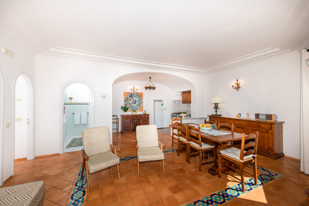 На фото: большая гостиная-столовая в средиземноморском стиле с белыми стенами, многоуровневым потолком, полом из терракотовой плитки и коричневым полом с