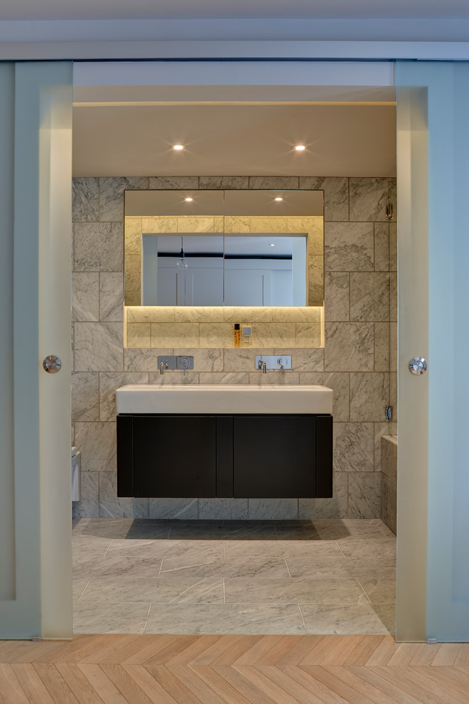 Small transitional master bathroom in London with white tile, stone tile, marble floors, shaker cabinets, black cabinets, a drop-in tub, a shower/bathtub combo, a wall-mount toilet, grey walls, a drop-in sink, marble benchtops, grey floor, a hinged shower door, grey benchtops, an enclosed toilet, a double vanity and a floating vanity.