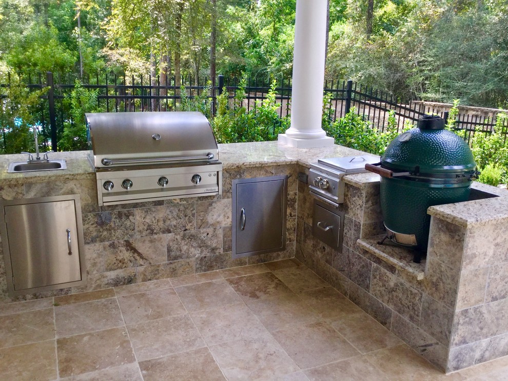 This is an example of a mid-sized transitional backyard patio in Houston with an outdoor kitchen, natural stone pavers and a pergola.