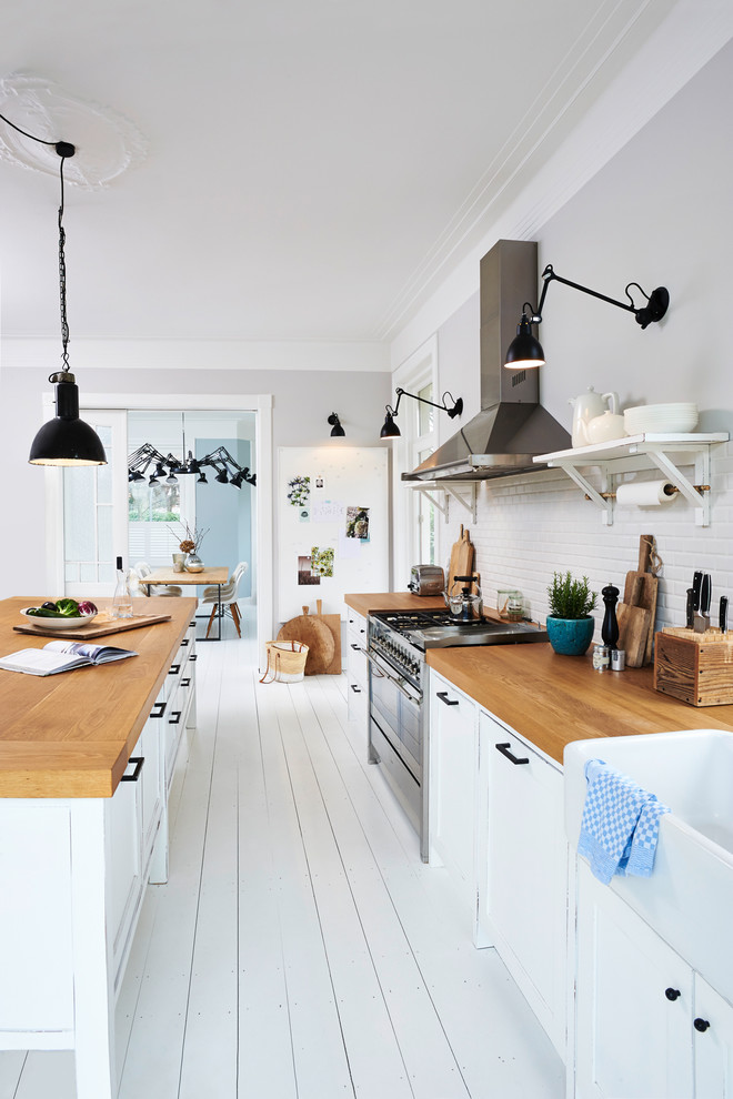 Photo of a mid-sized country single-wall open plan kitchen in Hamburg with a farmhouse sink, shaker cabinets, white cabinets, wood benchtops, white splashback, subway tile splashback, stainless steel appliances, painted wood floors, with island and white floor.