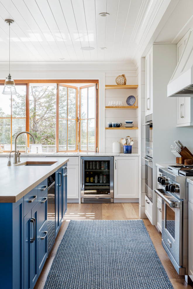 Large beach style l-shaped eat-in kitchen in Boston with a single-bowl sink, recessed-panel cabinets, white cabinets, granite benchtops, blue splashback, glass tile splashback, stainless steel appliances, medium hardwood floors, with island, white benchtop and timber.