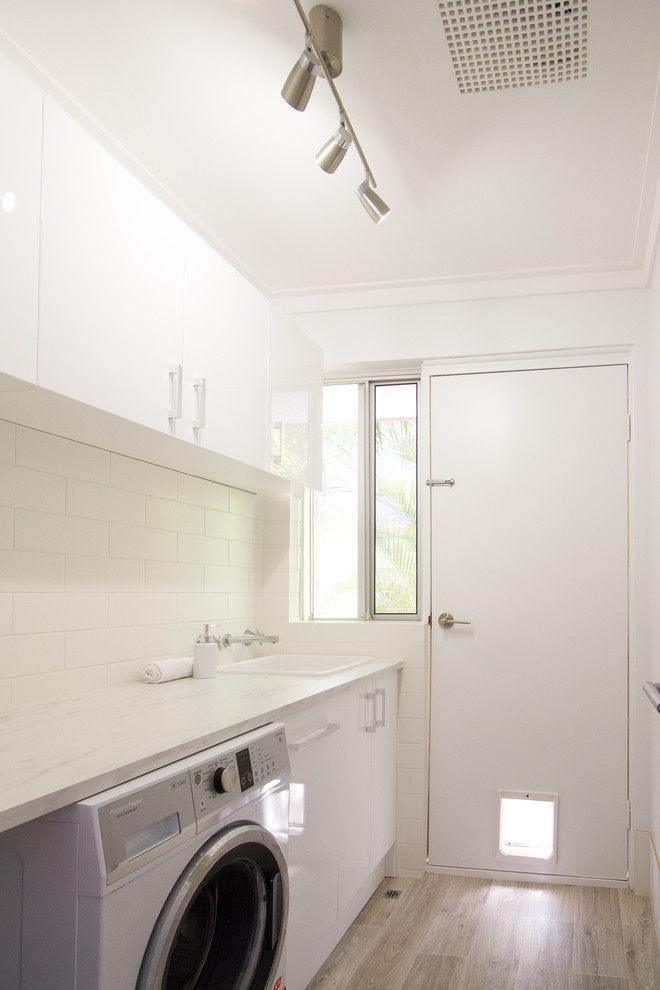 Small beach style single-wall dedicated laundry room in Perth with a drop-in sink, white cabinets, laminate benchtops, white walls, vinyl floors and a side-by-side washer and dryer.