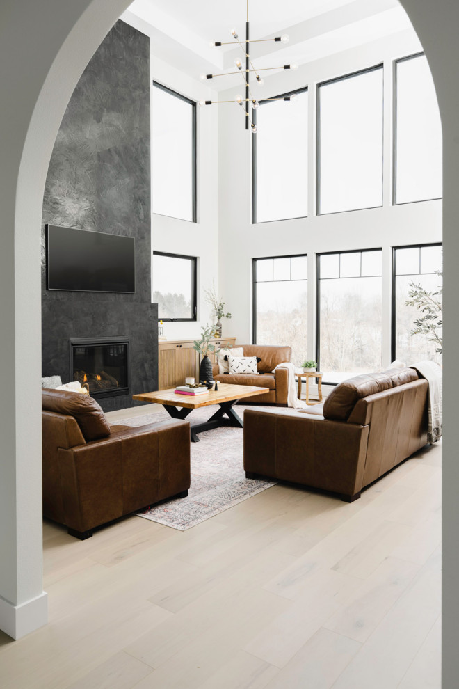 Modern open concept living room in Cedar Rapids with light hardwood floors, a standard fireplace, a plaster fireplace surround, a wall-mounted tv and vaulted.