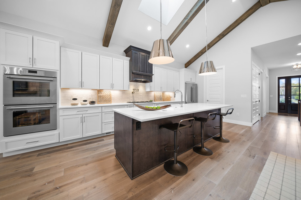 Transitional galley medium tone wood floor and vaulted ceiling open concept kitchen photo in Cincinnati with an undermount sink, shaker cabinets, white cabinets, quartz countertops, white backsplash, ceramic backsplash, stainless steel appliances, an island and white countertops