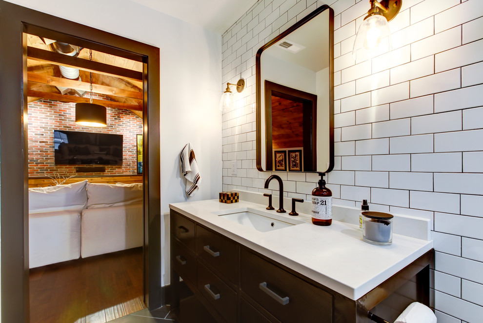 Mid-sized industrial bathroom in Raleigh with furniture-like cabinets, black cabinets, a wall-mount toilet, white tile, subway tile, white walls, porcelain floors, an undermount sink, engineered quartz benchtops, brown floor, a hinged shower door and an alcove shower.