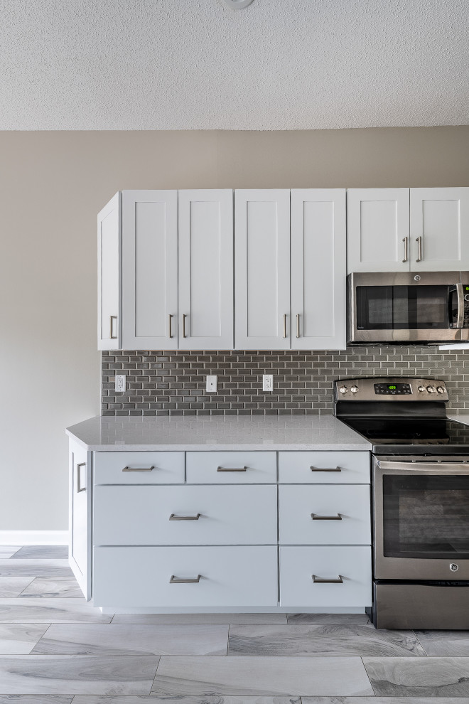 Example of a mid-sized transitional galley porcelain tile and multicolored floor eat-in kitchen design with an undermount sink, recessed-panel cabinets, white cabinets, quartz countertops, gray backsplash, ceramic backsplash, stainless steel appliances, a peninsula and white countertops