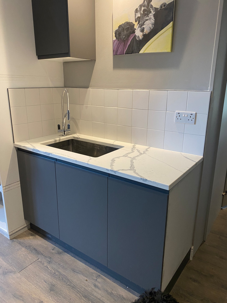 Inspiration for a large contemporary galley utility room in London with a drop-in sink, flat-panel cabinets, grey cabinets, quartzite benchtops, white splashback, porcelain splashback, beige walls, laminate floors, a side-by-side washer and dryer, grey floor and multi-coloured benchtop.