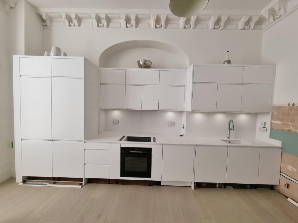 Foto på ett stort funkis vit linjärt kök med öppen planlösning, med en nedsänkt diskho, släta luckor, vita skåp, bänkskiva i kvartsit, vitt stänkskydd, stänkskydd i sten, vita vitvaror och målat trägolv