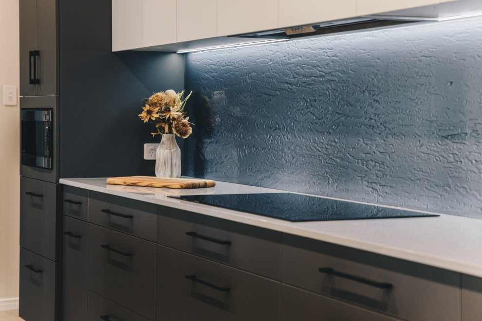 Inspiration for a large modern kitchen pantry in Brisbane with a drop-in sink, flat-panel cabinets, grey cabinets, quartz benchtops, grey splashback, glass sheet splashback, black appliances, porcelain floors, with island, grey floor and grey benchtop.
