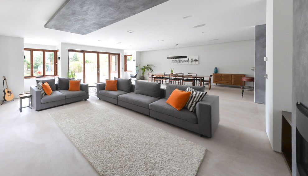 This is an example of a large contemporary open concept living room in Sussex with grey walls, concrete floors, a standard fireplace, a plaster fireplace surround and a built-in media wall.