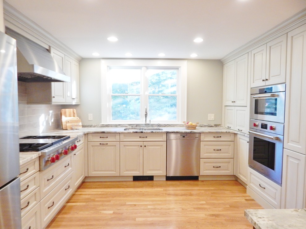 Inspiration for a mid-sized transitional l-shaped light wood floor open concept kitchen remodel in Boston with an undermount sink, raised-panel cabinets, white cabinets, quartzite countertops, stainless steel appliances and an island
