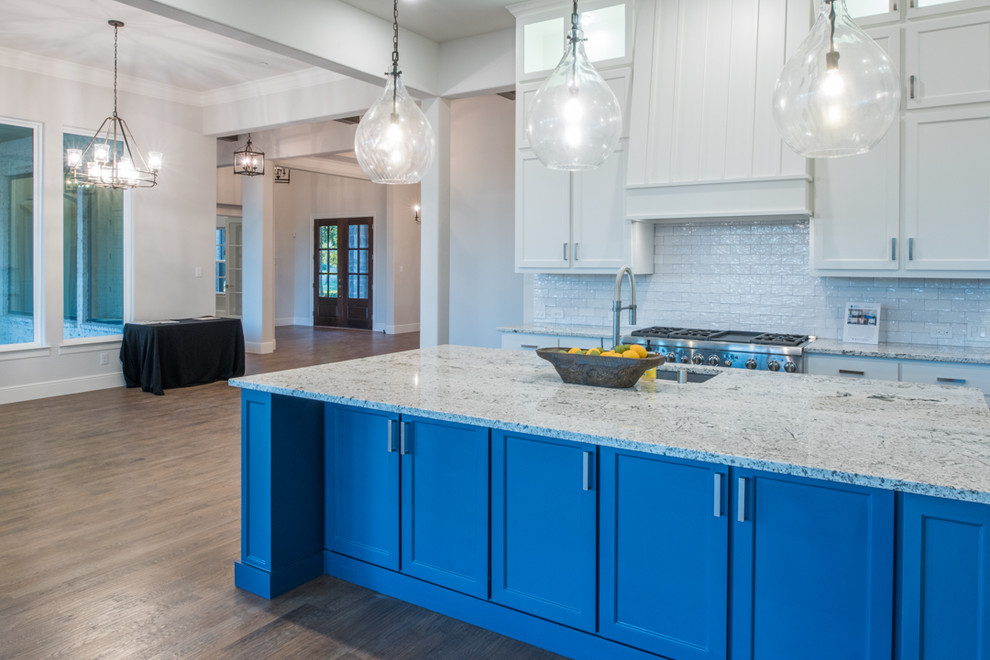 Large transitional medium tone wood floor and brown floor eat-in kitchen photo in Dallas with a drop-in sink, recessed-panel cabinets, white cabinets, wood countertops, white backsplash, ceramic backsplash, stainless steel appliances, an island and white countertops