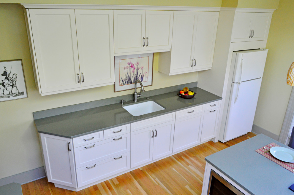 Inspiration for a mid-sized transitional light wood floor enclosed kitchen remodel in Seattle with an undermount sink, recessed-panel cabinets, white cabinets, quartz countertops, green backsplash, stone slab backsplash, white appliances and a peninsula