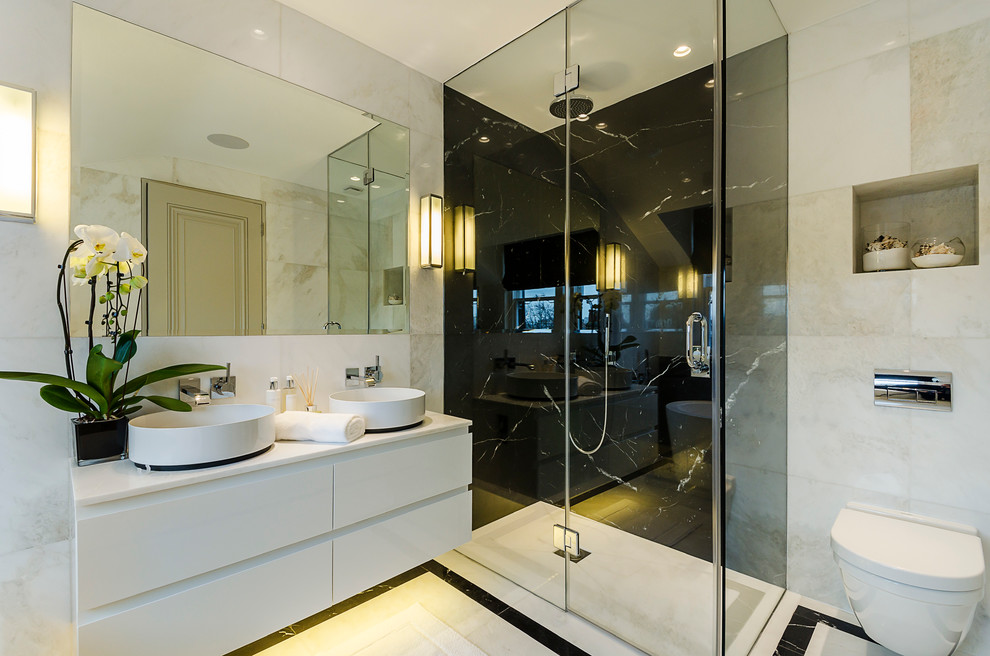 Inspiration for a large contemporary master bathroom in London with white cabinets, marble benchtops, a freestanding tub, a curbless shower, a wall-mount toilet, black and white tile, stone tile, white walls, marble floors, a vessel sink and flat-panel cabinets.