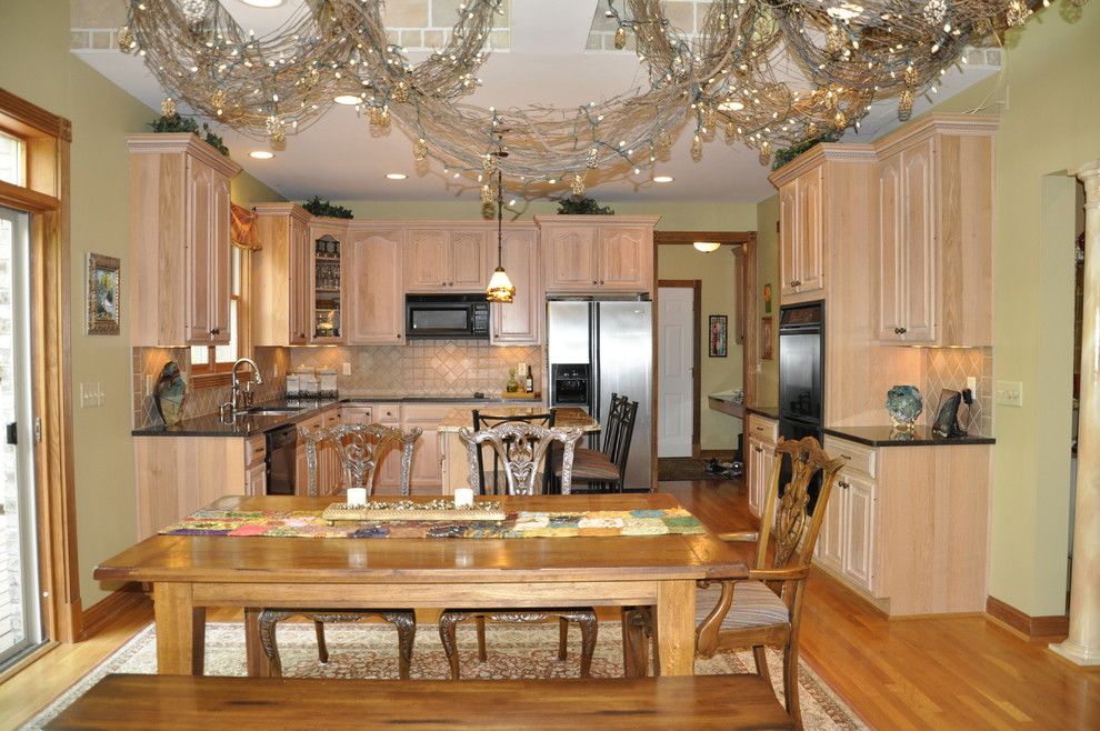 Example of a mid-sized transitional u-shaped medium tone wood floor eat-in kitchen design in Cincinnati with an undermount sink, raised-panel cabinets, light wood cabinets, granite countertops, beige backsplash, porcelain backsplash, black appliances, green walls and an island
