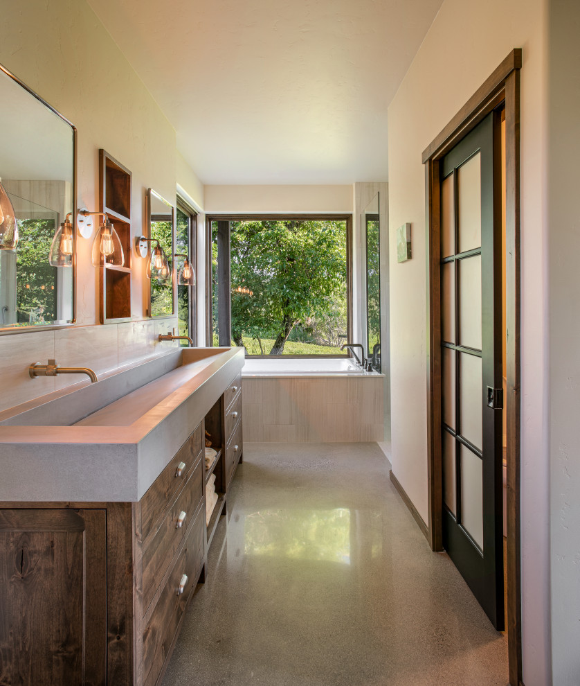 This is an example of a mid-sized contemporary master bathroom in Seattle with flat-panel cabinets, medium wood cabinets, a drop-in tub, an open shower, beige tile, beige walls, concrete floors, a trough sink, concrete benchtops, an open shower, an enclosed toilet and a built-in vanity.