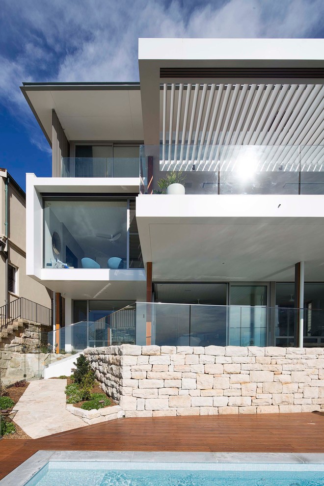 This is an example of a large beach style three-storey white house exterior in Sydney with concrete fiberboard siding, a flat roof and a metal roof.
