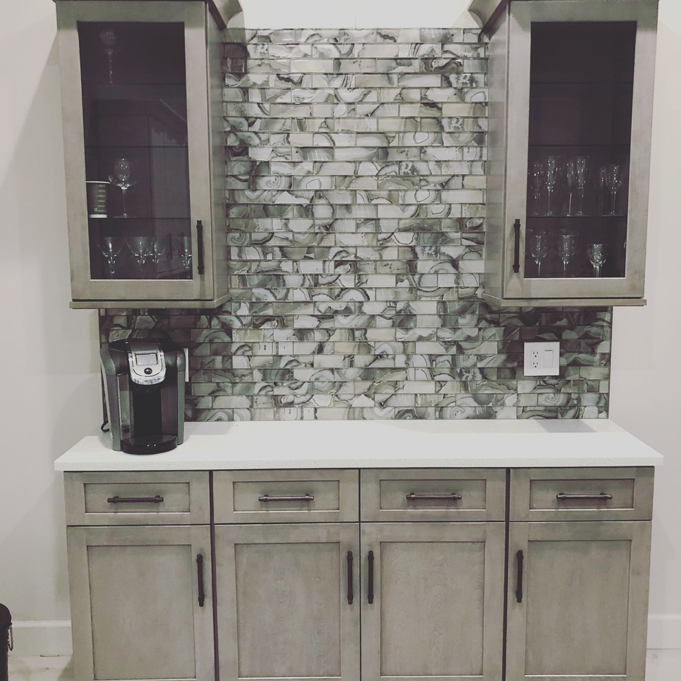 This is an example of a small contemporary single-wall bar cart in Miami with no sink, shaker cabinets, grey cabinets, granite benchtops, multi-coloured splashback, glass tile splashback, light hardwood floors, grey floor and white benchtop.