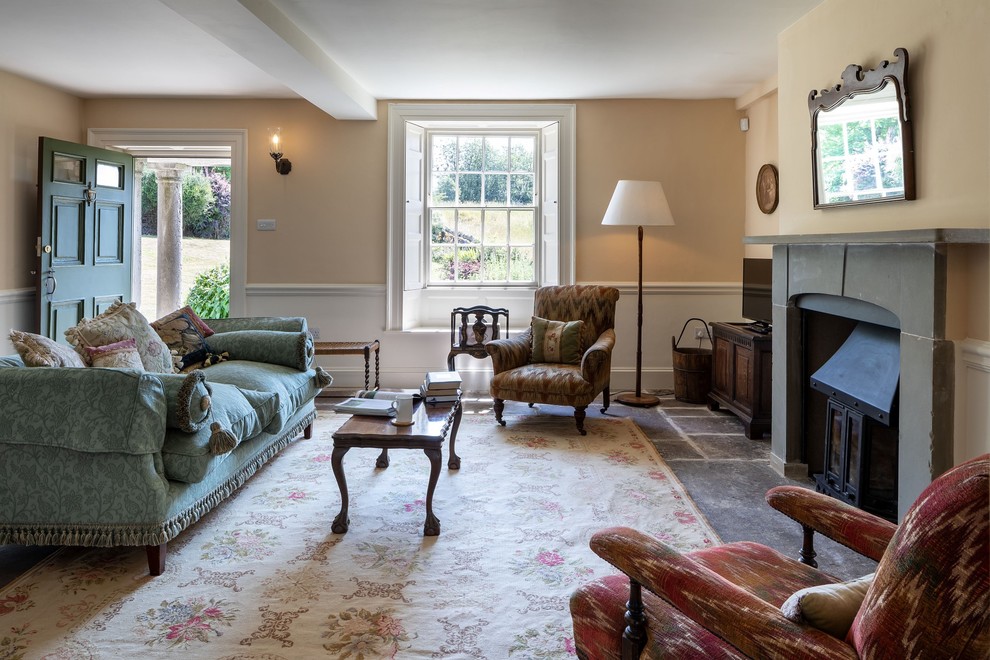 Photo of a large country formal enclosed living room with beige walls, slate flooring, a wood burning stove, a stone fireplace surround, a freestanding tv and grey floors.