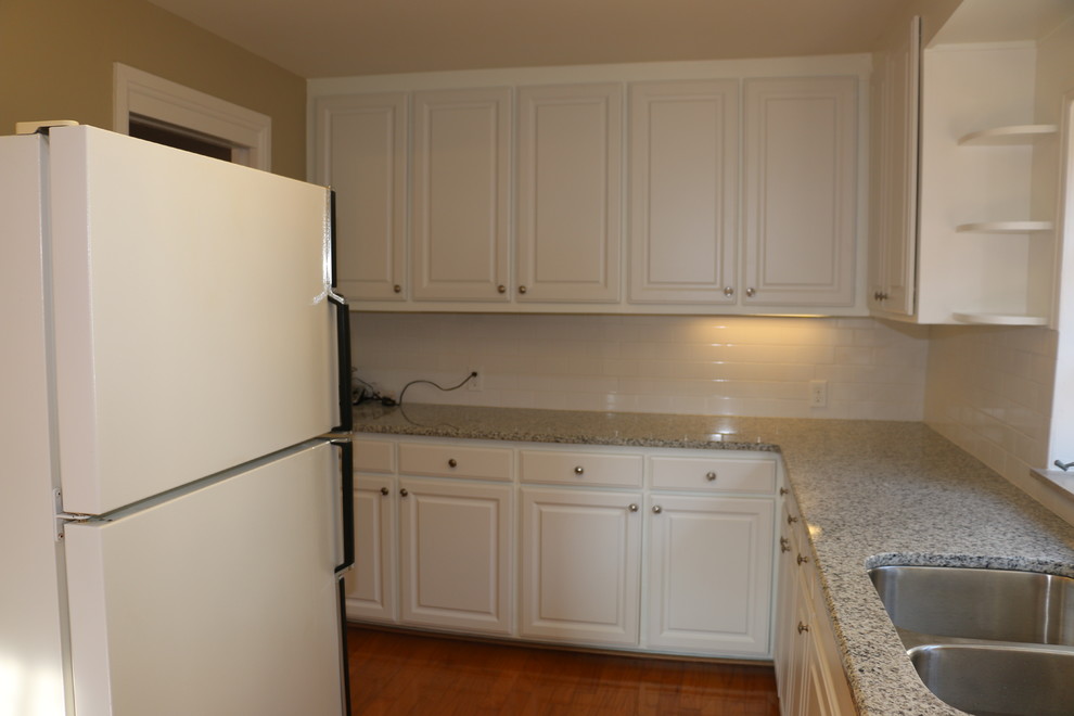 Mid-sized elegant l-shaped light wood floor eat-in kitchen photo with an undermount sink, raised-panel cabinets, white cabinets, granite countertops, white backsplash, ceramic backsplash and white appliances