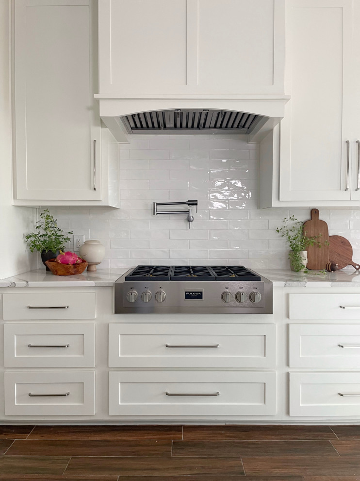 Example of a large ceramic tile and brown floor kitchen design in Austin with an undermount sink, shaker cabinets, white cabinets, white backsplash, subway tile backsplash, stainless steel appliances, an island and white countertops