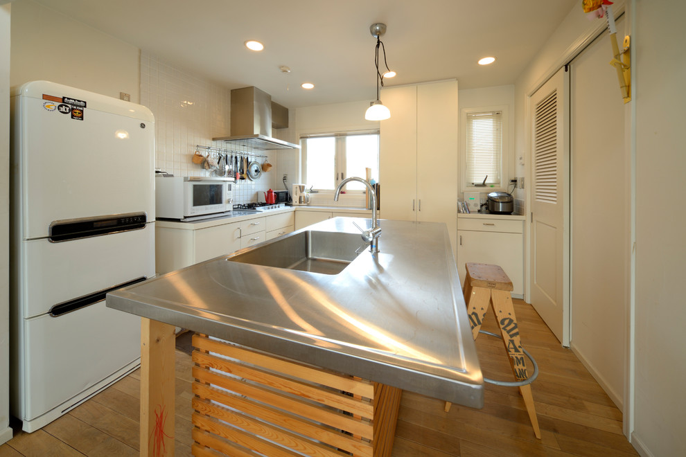 Asian l-shaped kitchen in Other with stainless steel benchtops, an integrated sink, flat-panel cabinets, white splashback, porcelain splashback, stainless steel appliances, light hardwood floors, with island and beige floor.