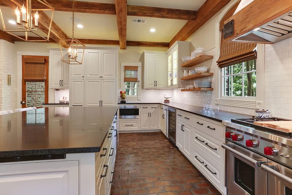 This is an example of a large country u-shaped kitchen pantry in New Orleans with an undermount sink, beaded inset cabinets, white cabinets, granite benchtops, white splashback, stainless steel appliances, brick floors, with island and subway tile splashback.