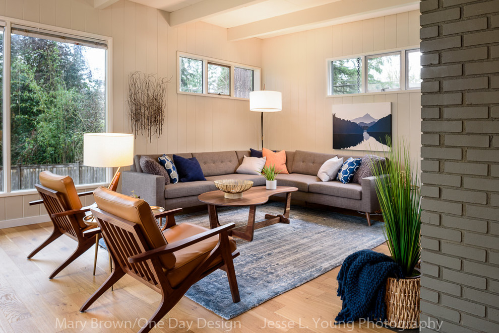 This is an example of a large midcentury open concept living room in Seattle with beige walls, light hardwood floors, a standard fireplace, a brick fireplace surround and a wall-mounted tv.